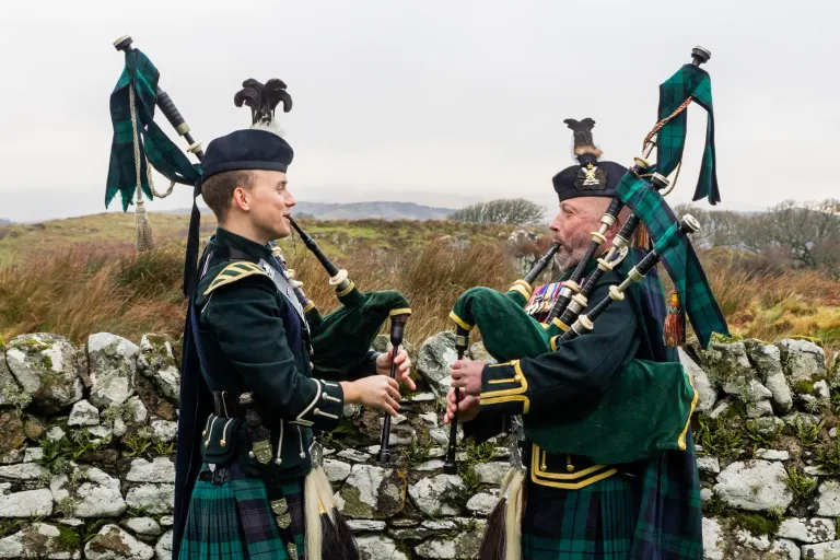 Gordon and Kyle Rowan playing bagpipes together in full Highland dress
